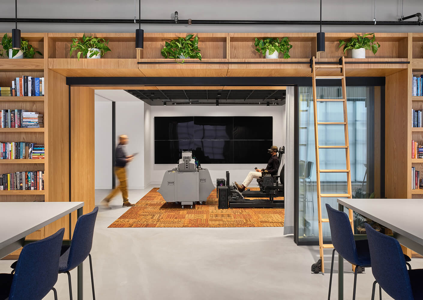 Modern office space with VR setup and bookshelves, featuring wooden accents and plants.