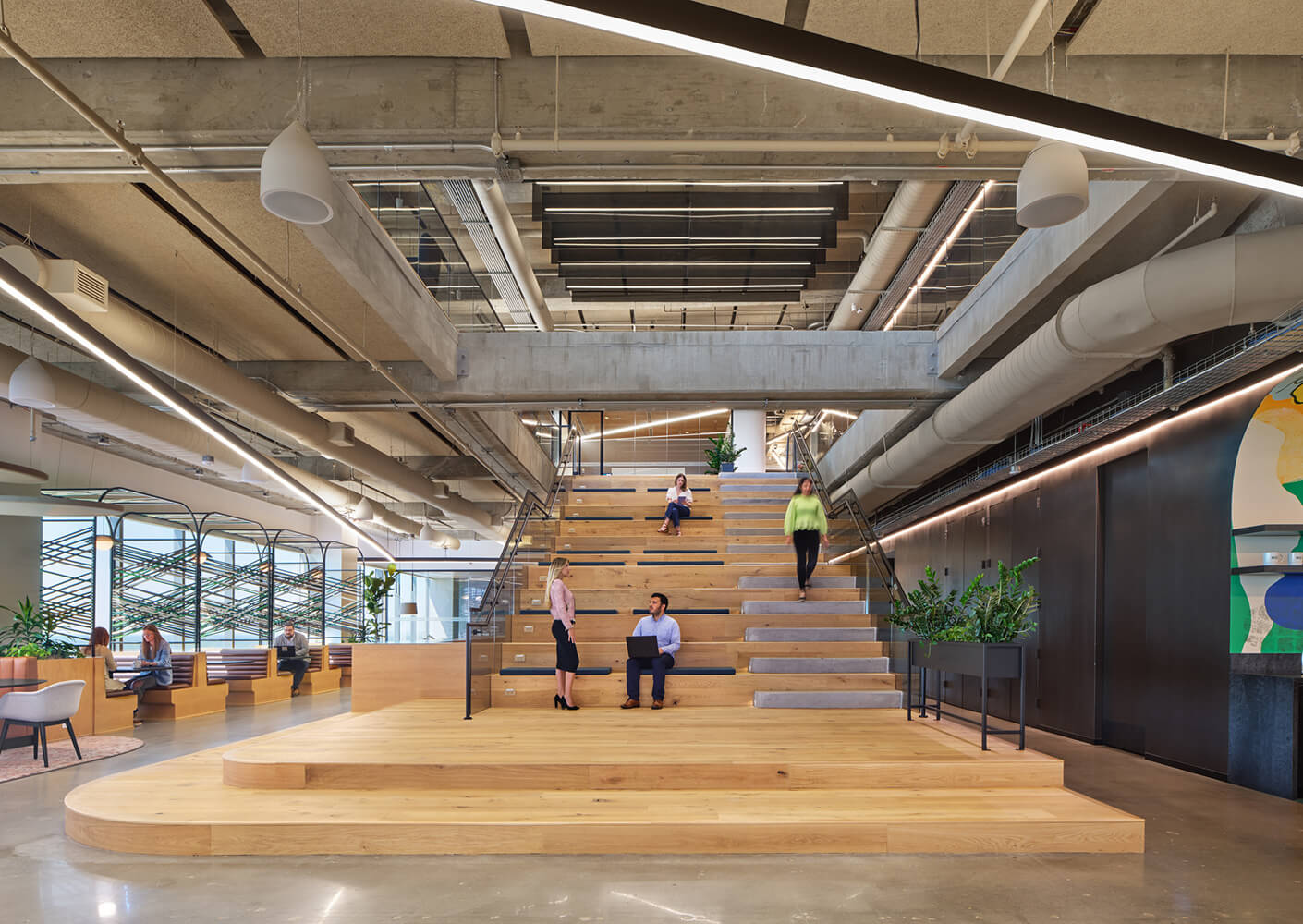 Modern office lobby with spacious wooden stairs and people interacting.