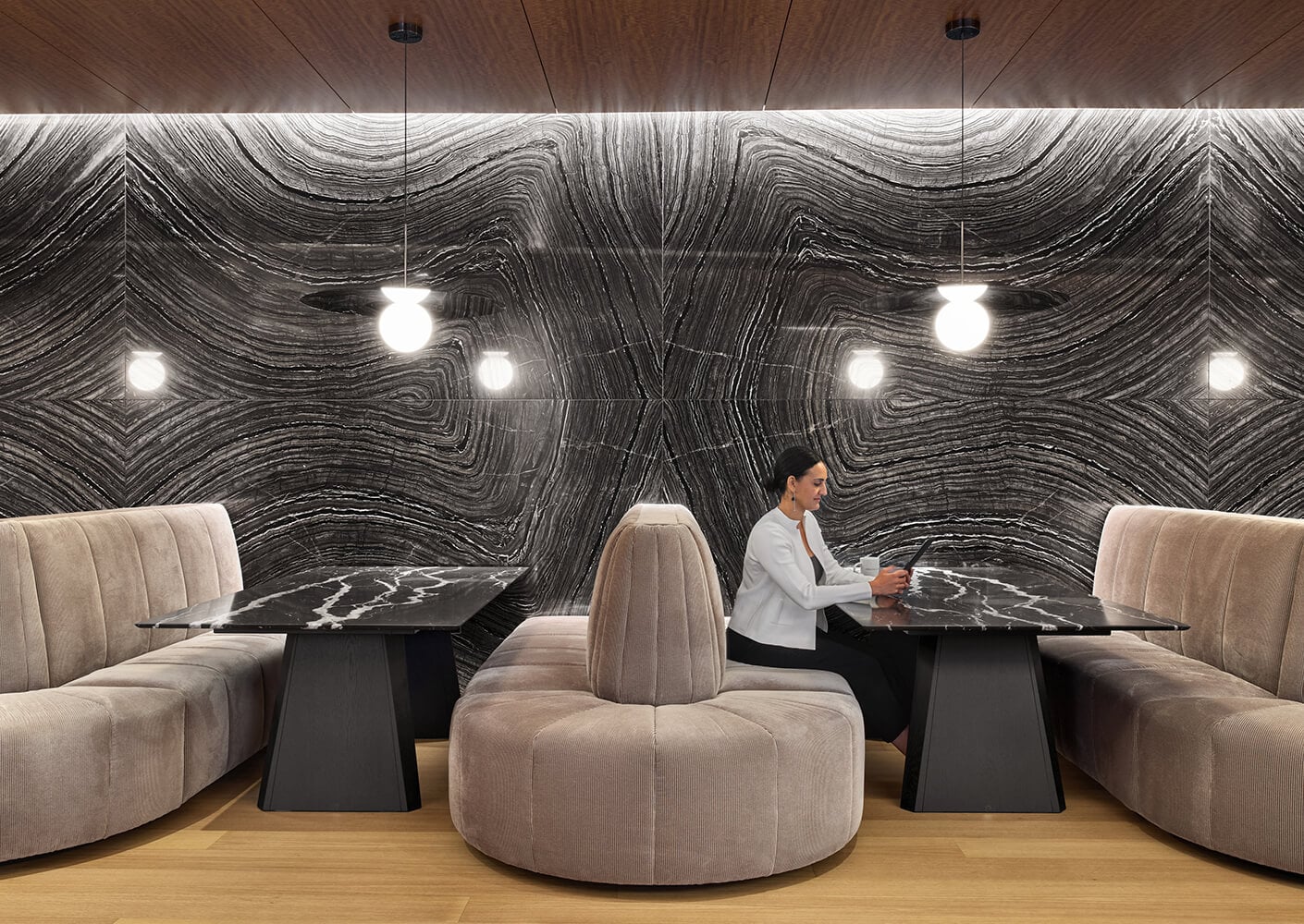 Modern lounge with marble wall, plush seating, and a person using a smartphone.