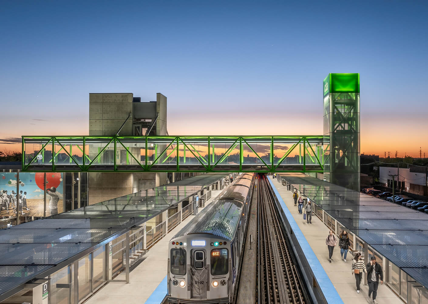 Modern train station at sunset with elevated walkway and passengers.