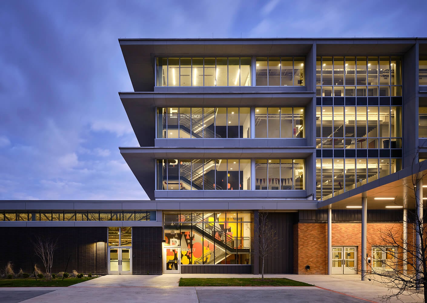 Modern school building exterior at dusk with illuminated windows.