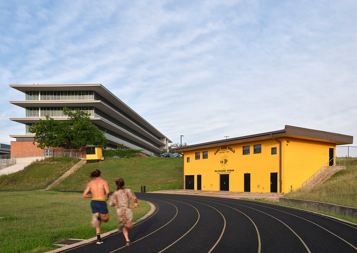 Two people jogging on a track by East Side Field building.