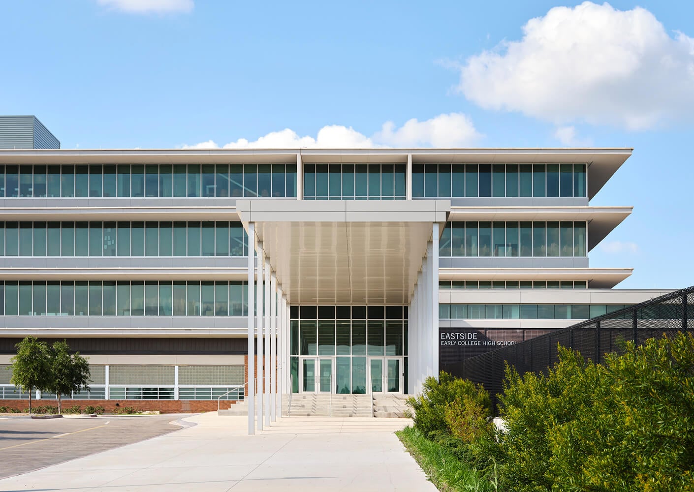 Modern school building with glass facade and entrance canopy under a blue sky.