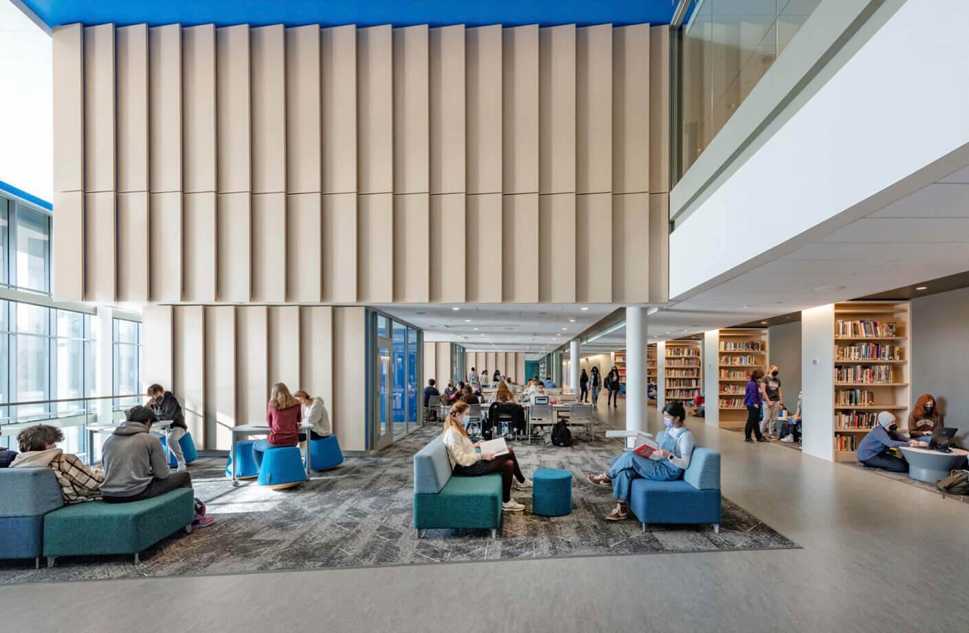 Modern library interior with students studying on sofas and browsing bookshelves.