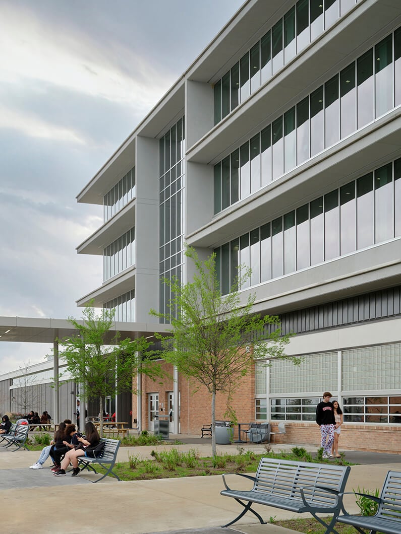 Modern academic building with students relaxing outside on benches.