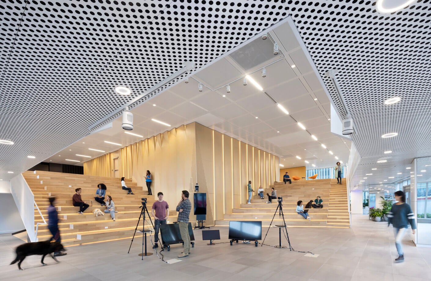 Modern open-space lounge with people, cameras, and seating on wooden steps.