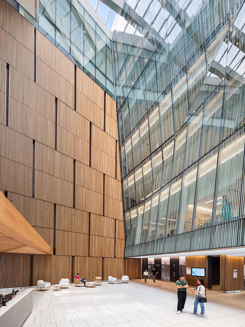Modern building atrium with wood panels and people walking, spacious and bright interior design.