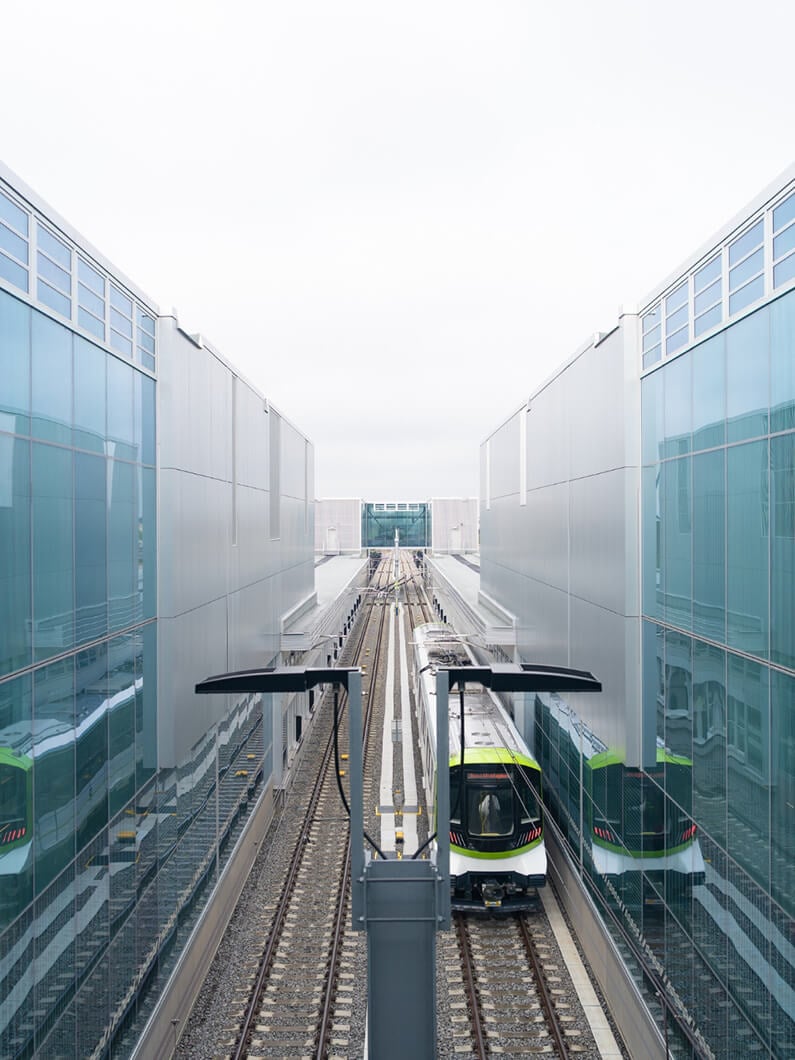 Modern train between glass buildings on tracks, skyward view.