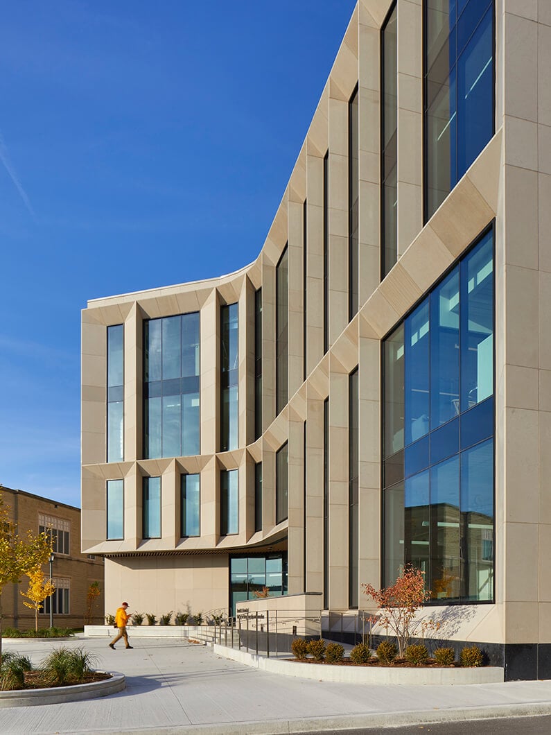 Contemporary building facade with large windows and a person walking nearby under clear blue sky.
