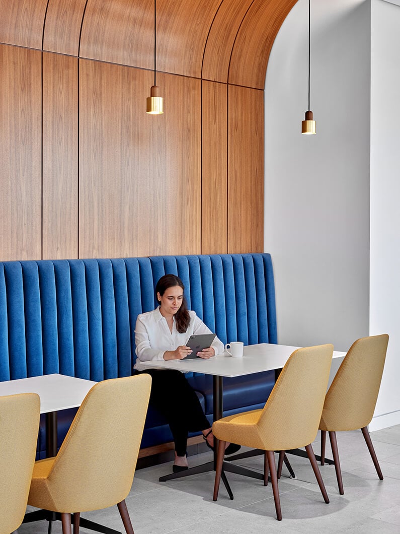 Woman reading tablet in modern cafe with blue seating and yellow chairs.