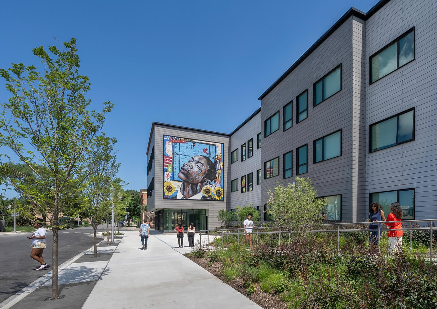 Modern building with mural art and people walking on a sunny day.