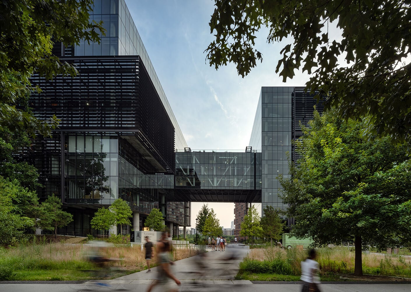 Modern glass building with sky bridge and lush green landscaping.