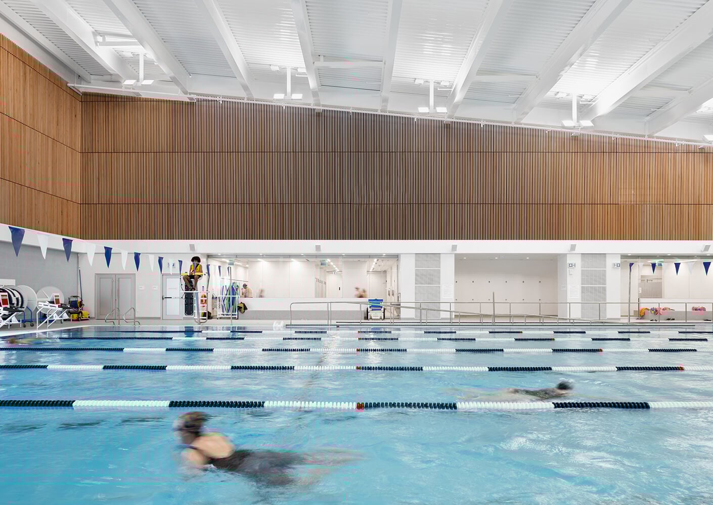 Indoor swimming pool with lanes and swimmers, lifeguard on duty.