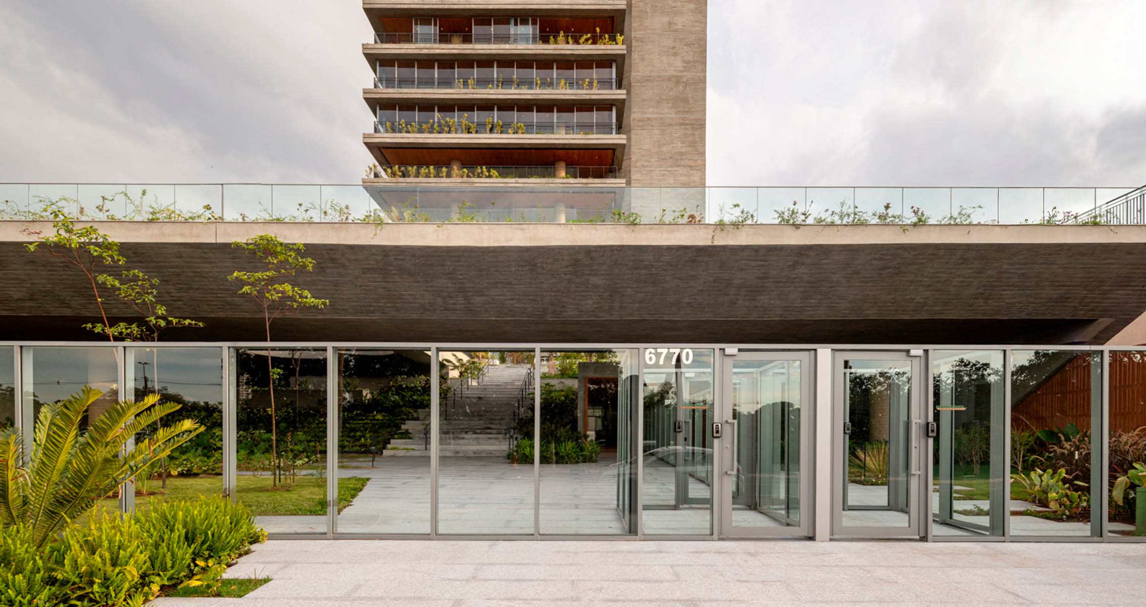 Modern building entrance with greenery and glass doors.
