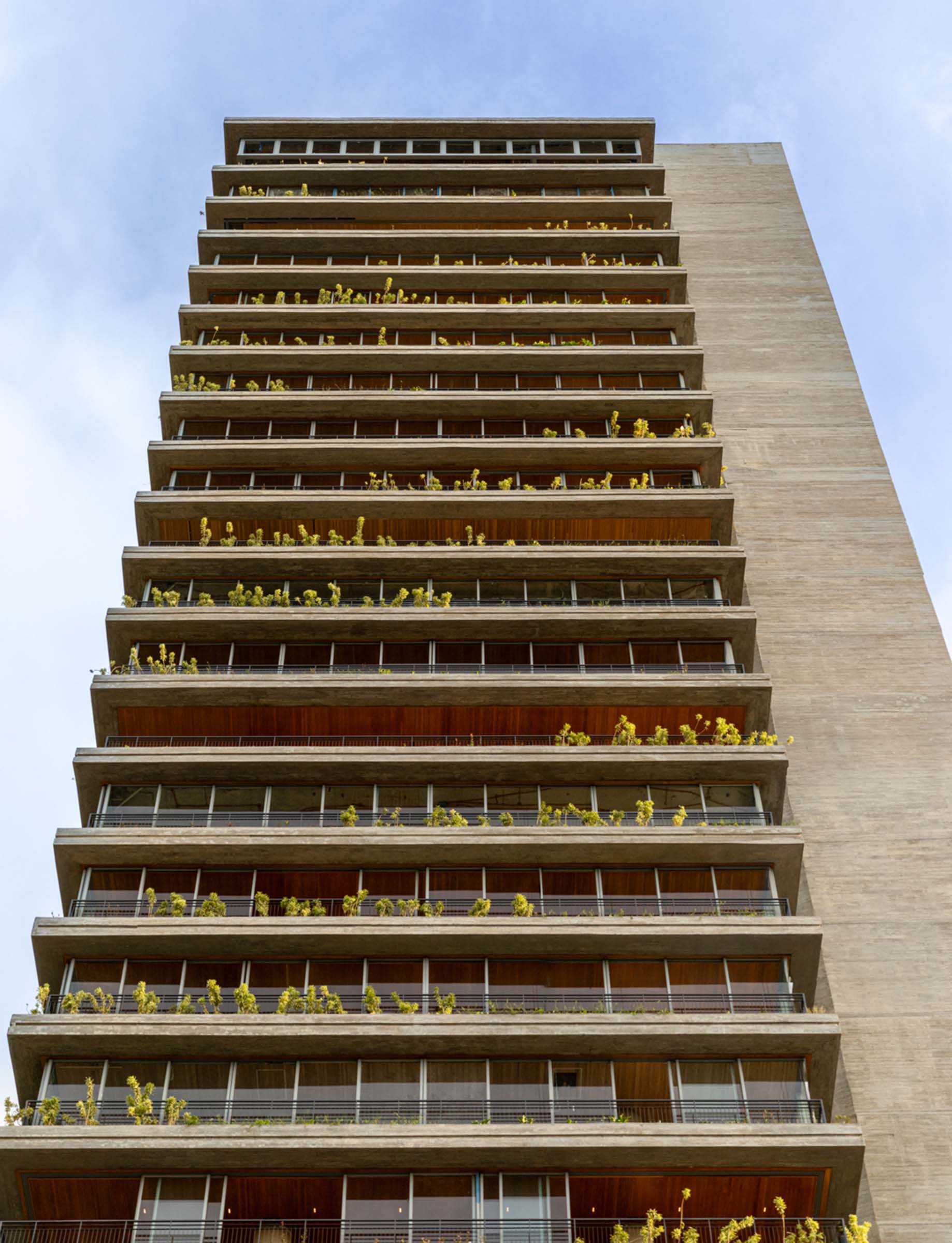 Modern high-rise building with green balconies and clear sky.