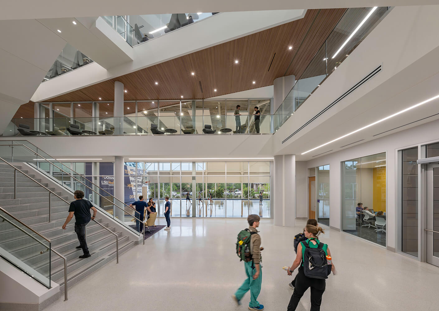 Modern atrium with people, glass railings, stairs, and natural light.