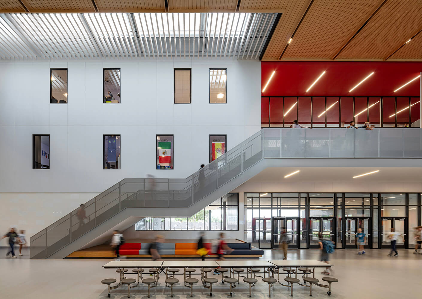 Modern school interior with stairs, students, and large windows.