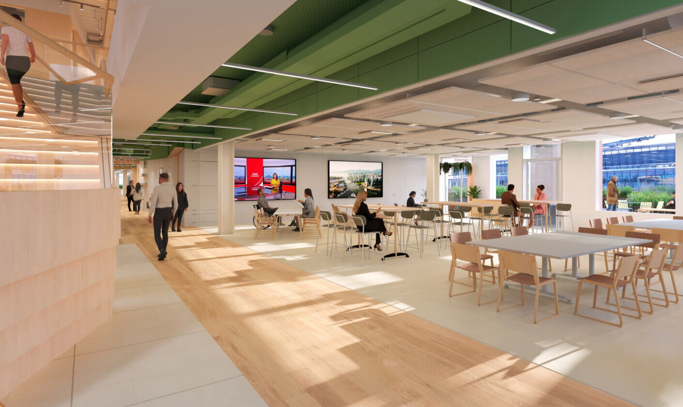 Modern open-plan office with people working and walking around, featuring large screens.