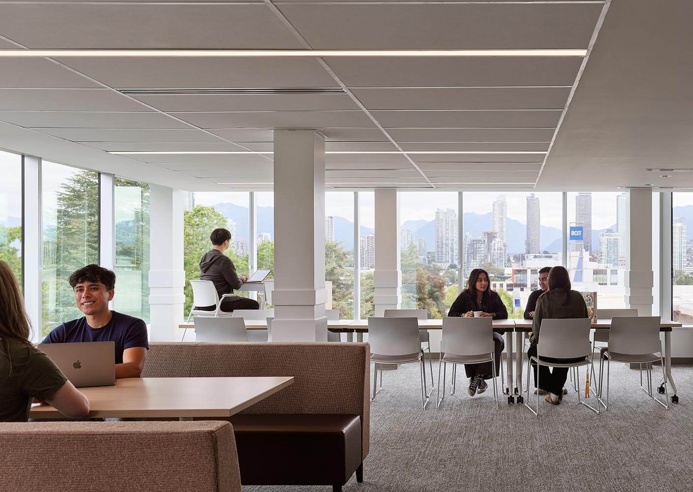 Modern office space with people working, large windows, city view.