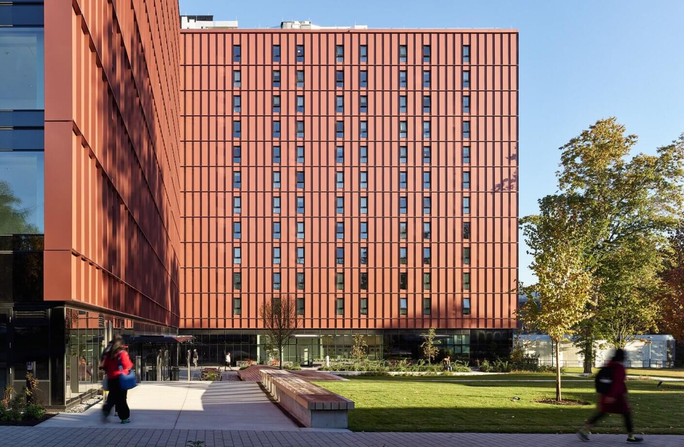 Modern red building with garden and people walking.