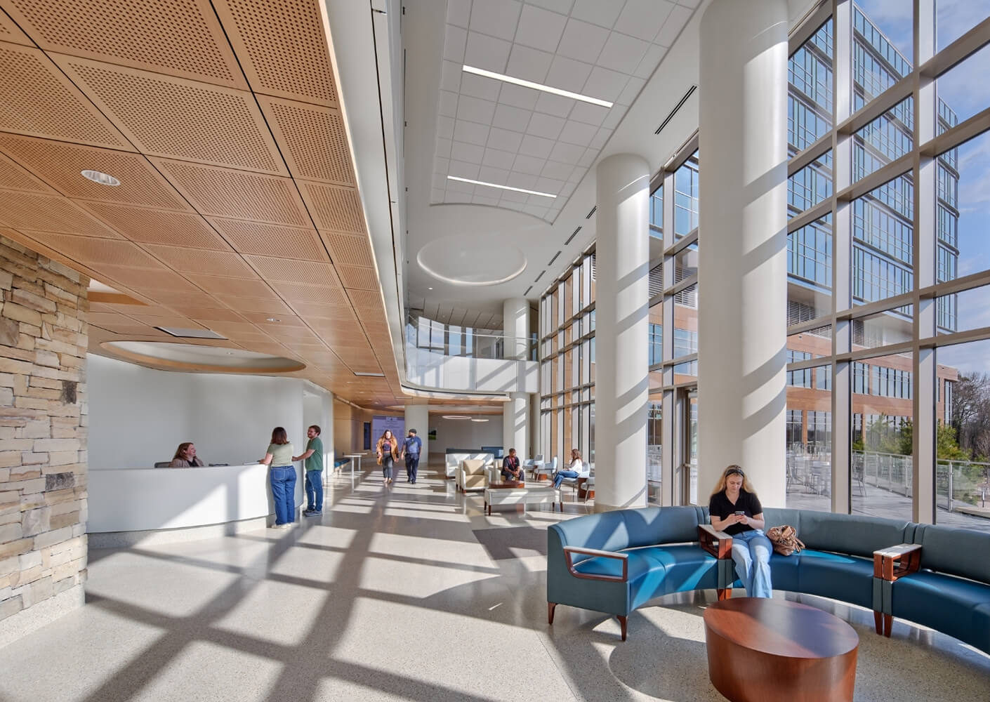 Modern lobby with tall windows, seating area, and people conversing and working.