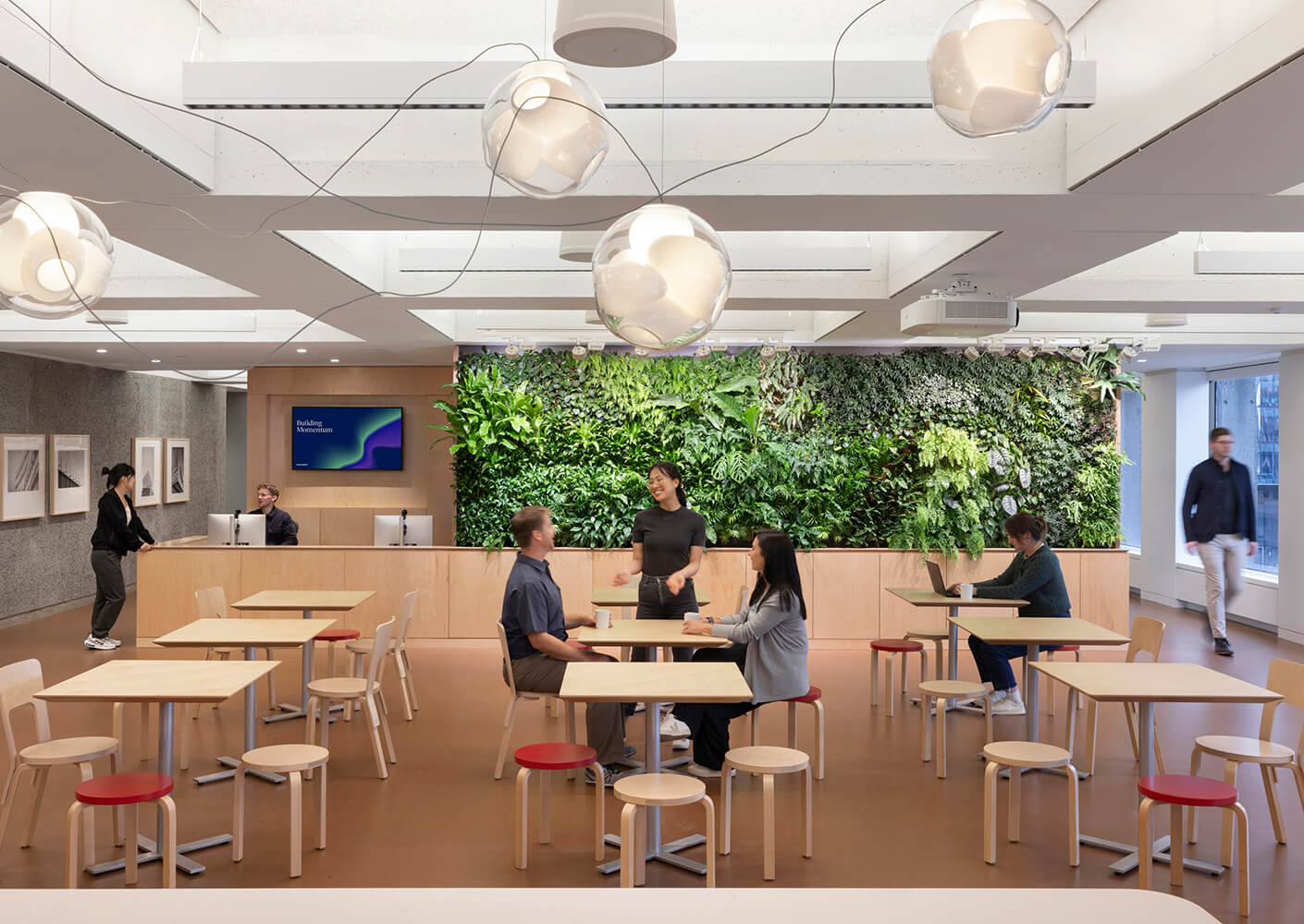 Modern office lounge with greenery wall and people interacting.