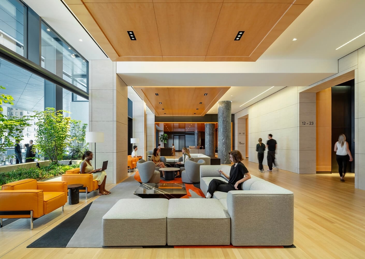 Modern office lobby with people seated on sofas, using laptops and phones.