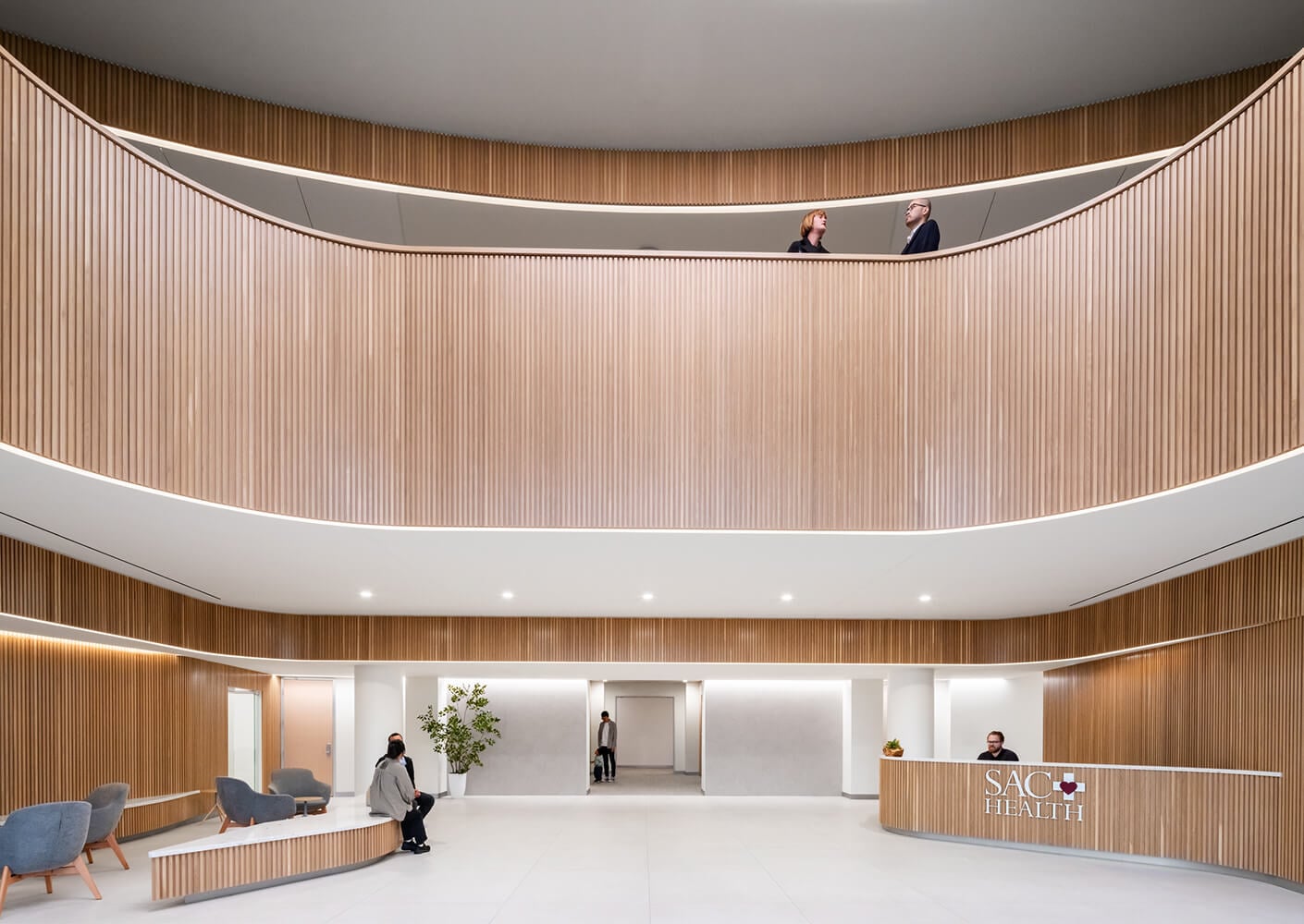 Modern healthcare lobby with wood paneling and people interacting, SAC Health reception.