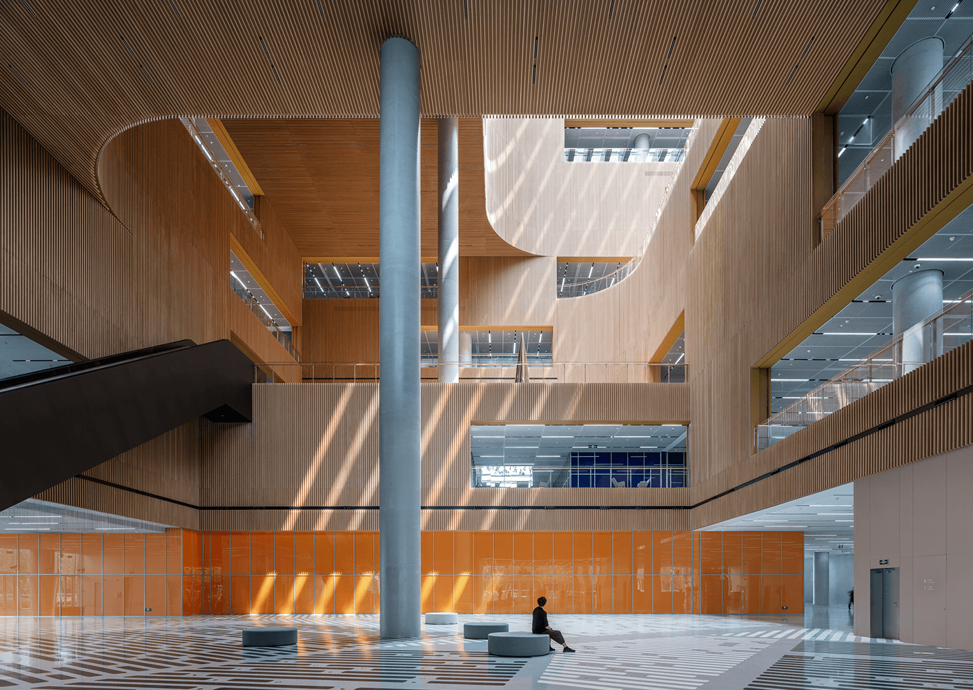 Modern atrium with wood panels and sunlight, featuring architectural details and seating.