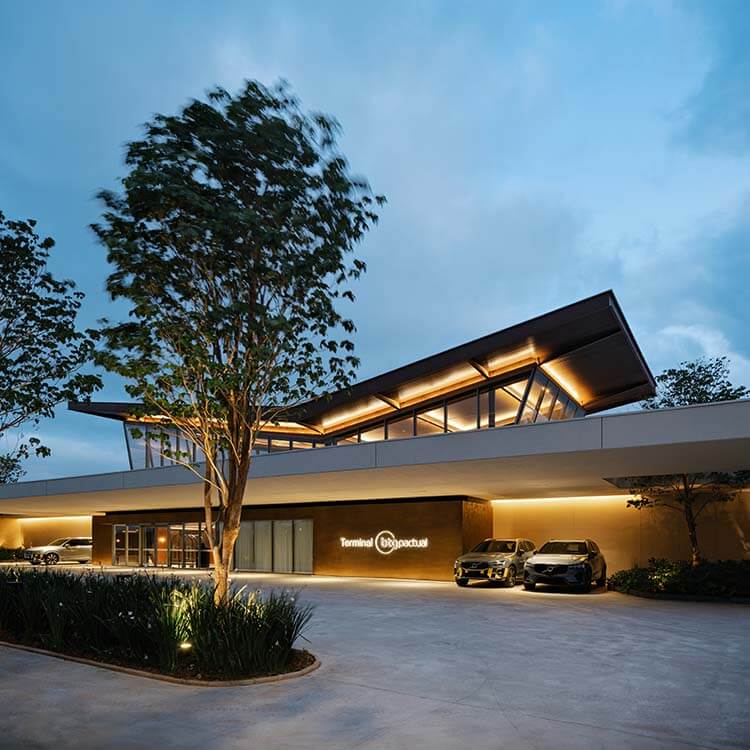 Modern building exterior lit at dusk with parked cars and trees.