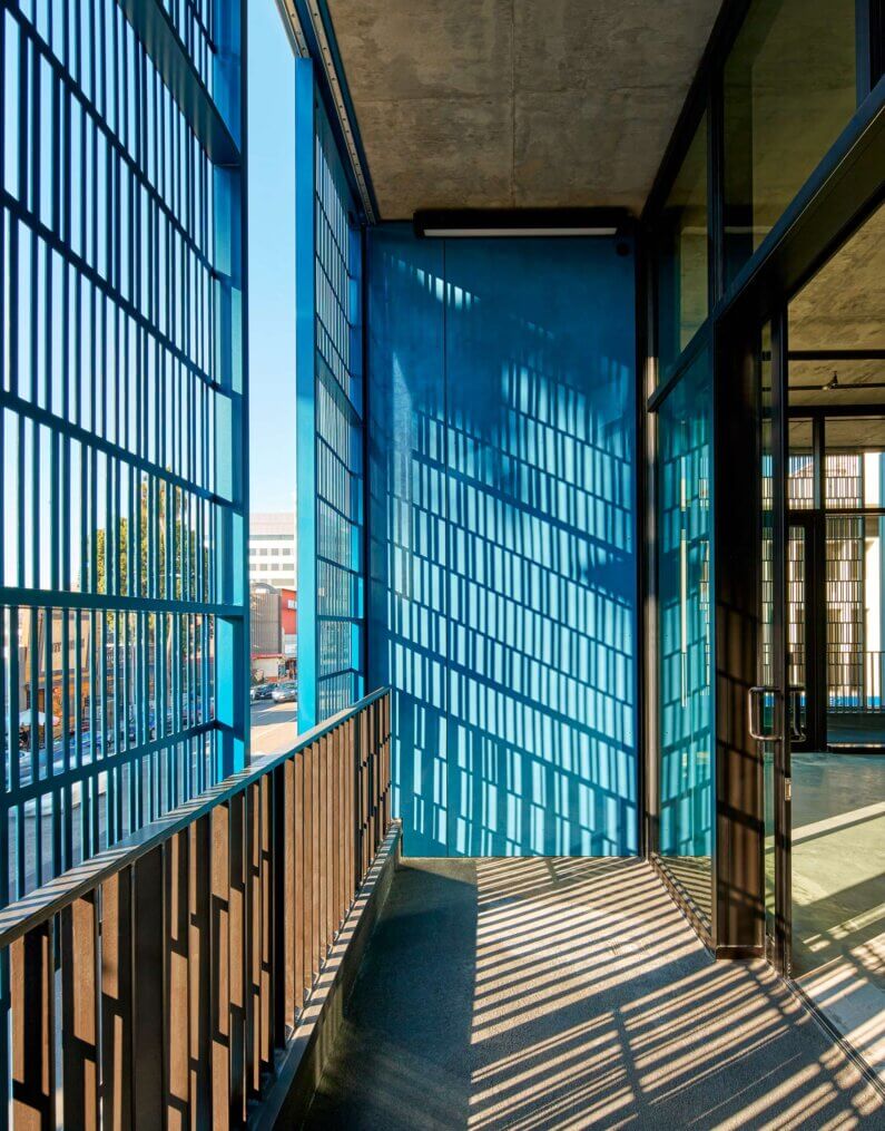 Modern balcony with blue grating, shadows casting geometric patterns on floor.
