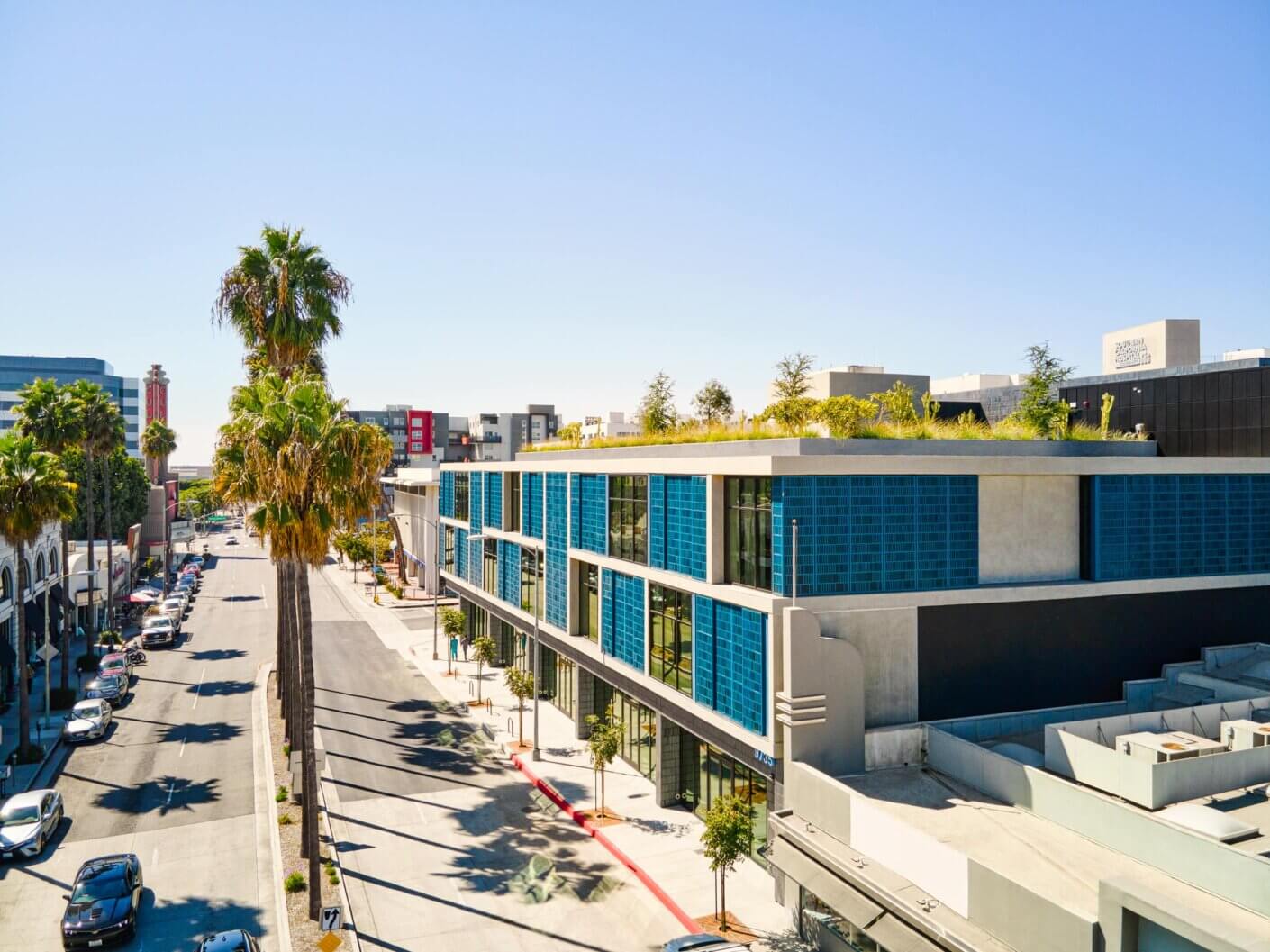 Modern urban street with palm trees and eco-friendly building, sunny blue sky.