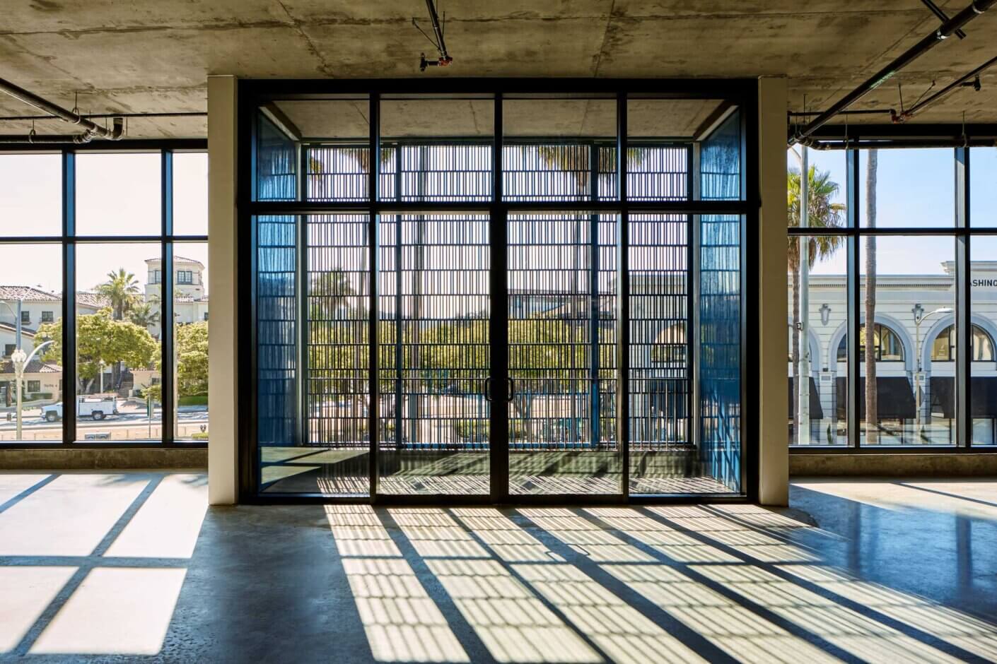 Sunlit modern building interior with large windows and grid pattern shadows.