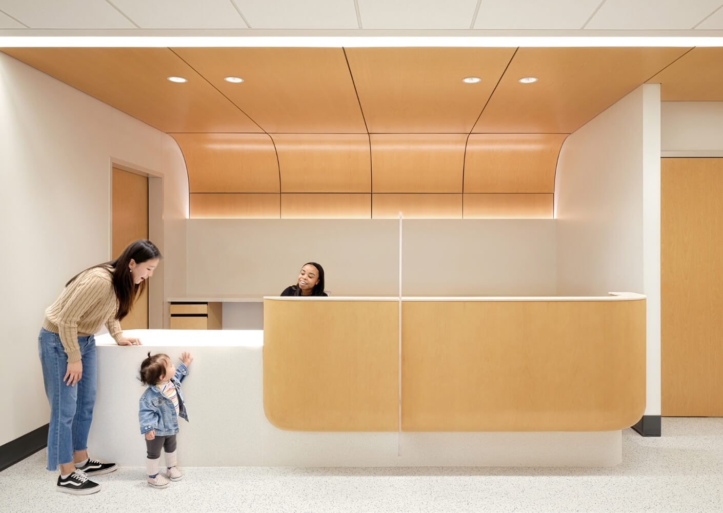Reception desk with mother, child, and smiling receptionist in modern, wood-accented office.