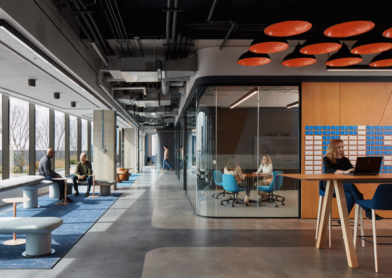 Modern office space with people collaborating and working in a bright, open layout.