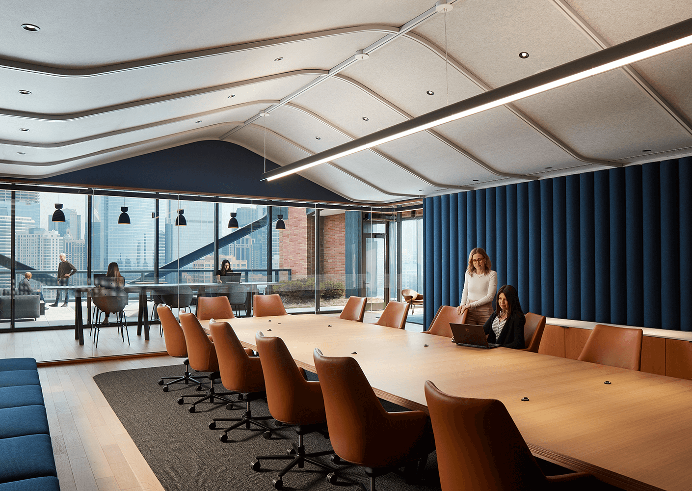 Modern boardroom with women collaborating on a laptop near a large window.