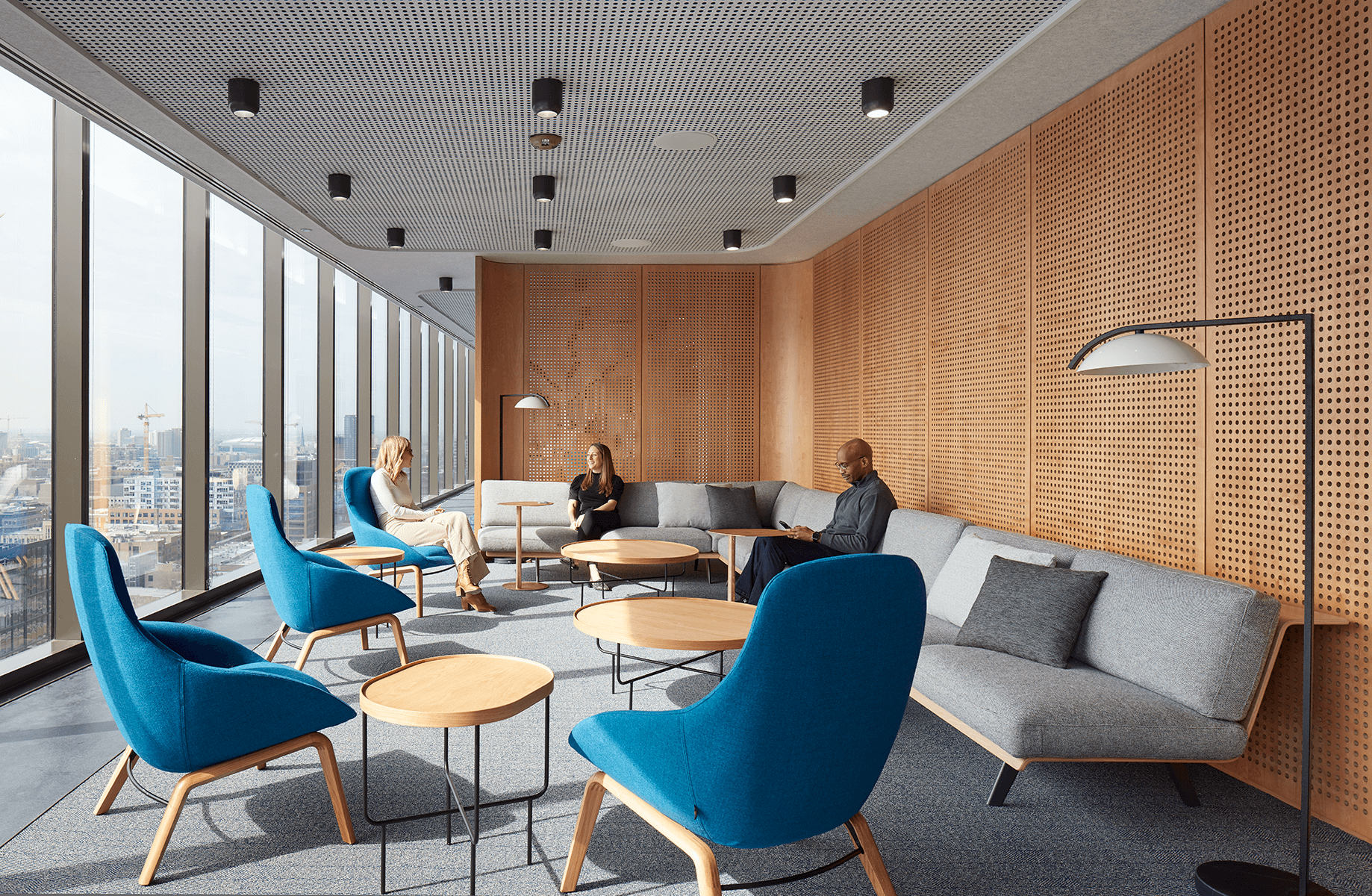 Modern office lounge with blue chairs, city view, and people conversing in natural light.