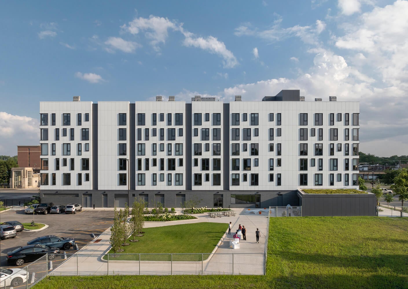 Modern apartment building with green space and parking area under a clear blue sky.