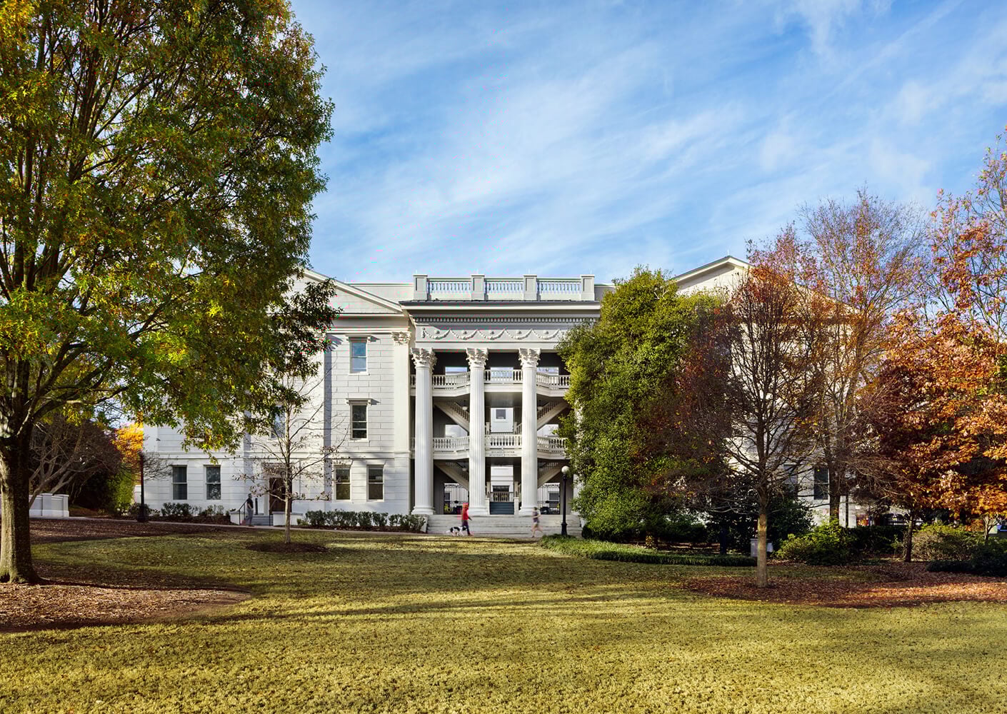 Historic white building with columns amidst trees and lawn on a sunny day.