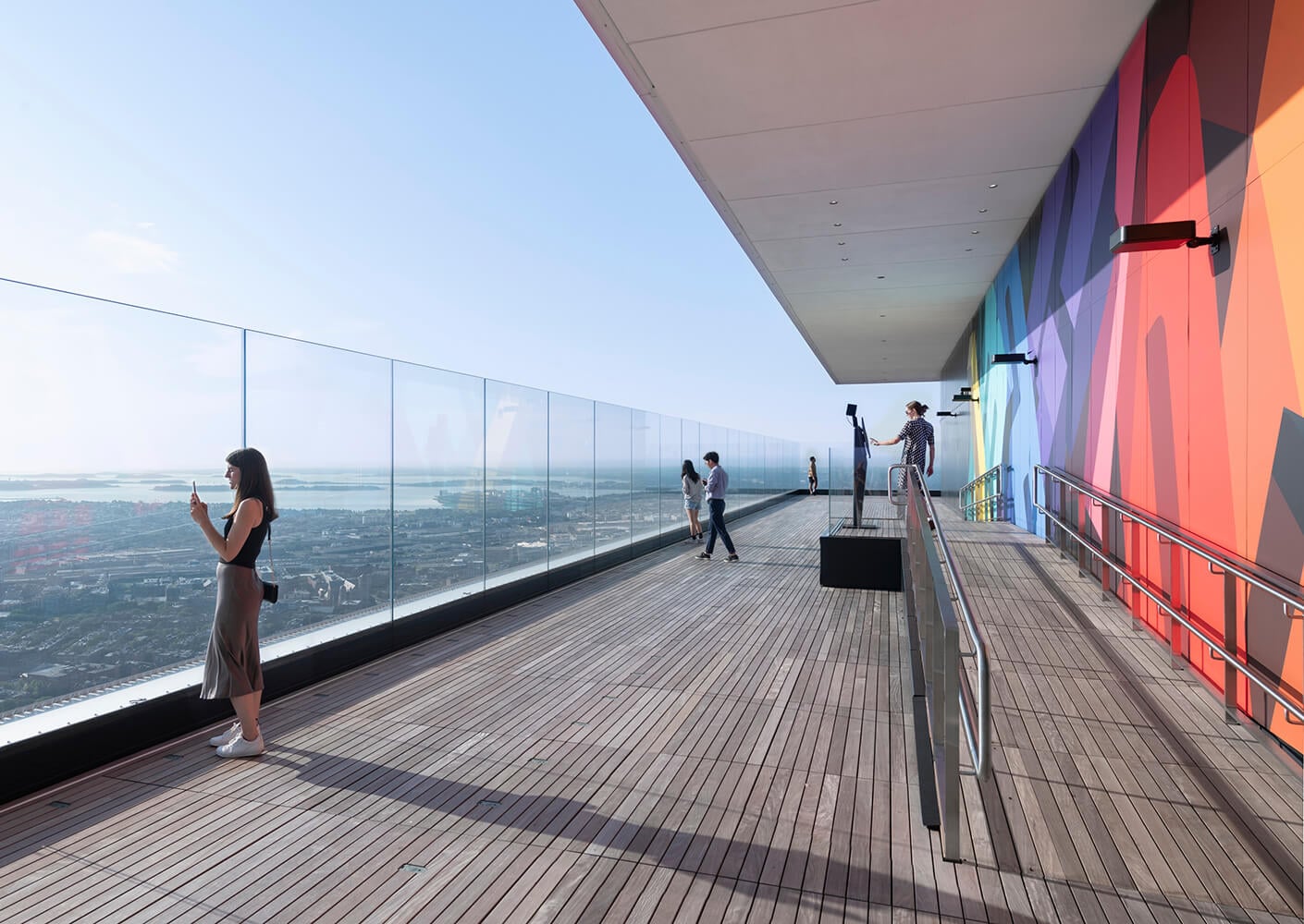 Rooftop observation deck with glass railings overlooking a cityscape under clear blue skies.