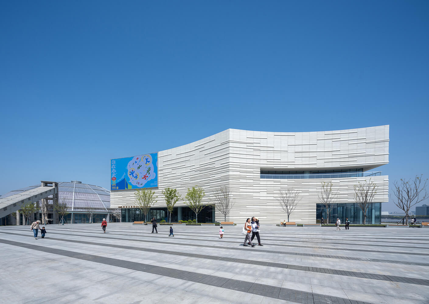Modern architectural building under clear blue sky with people walking in plaza.