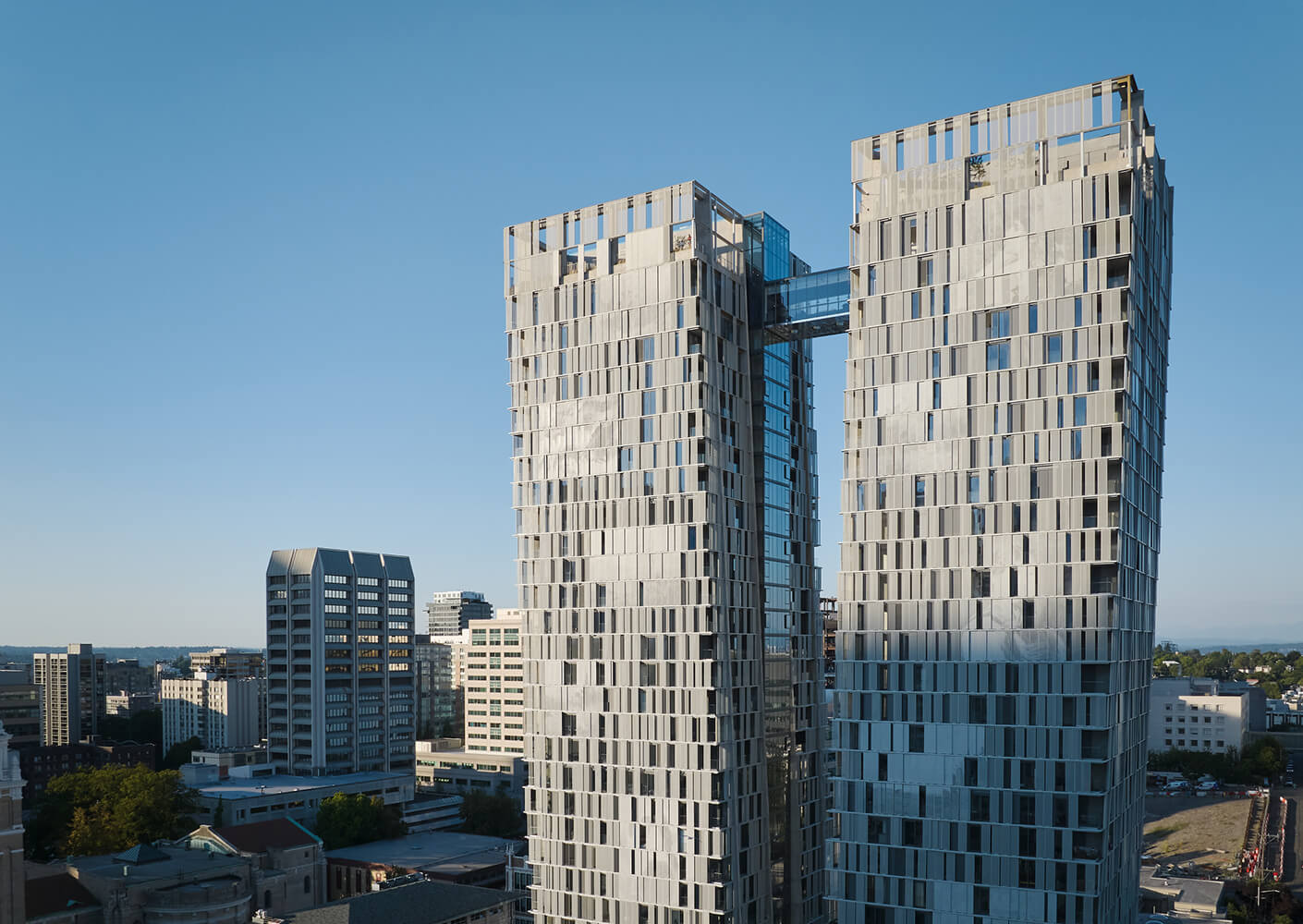 Twin modern skyscrapers with an upper sky bridge in an urban landscape under a clear blue sky.