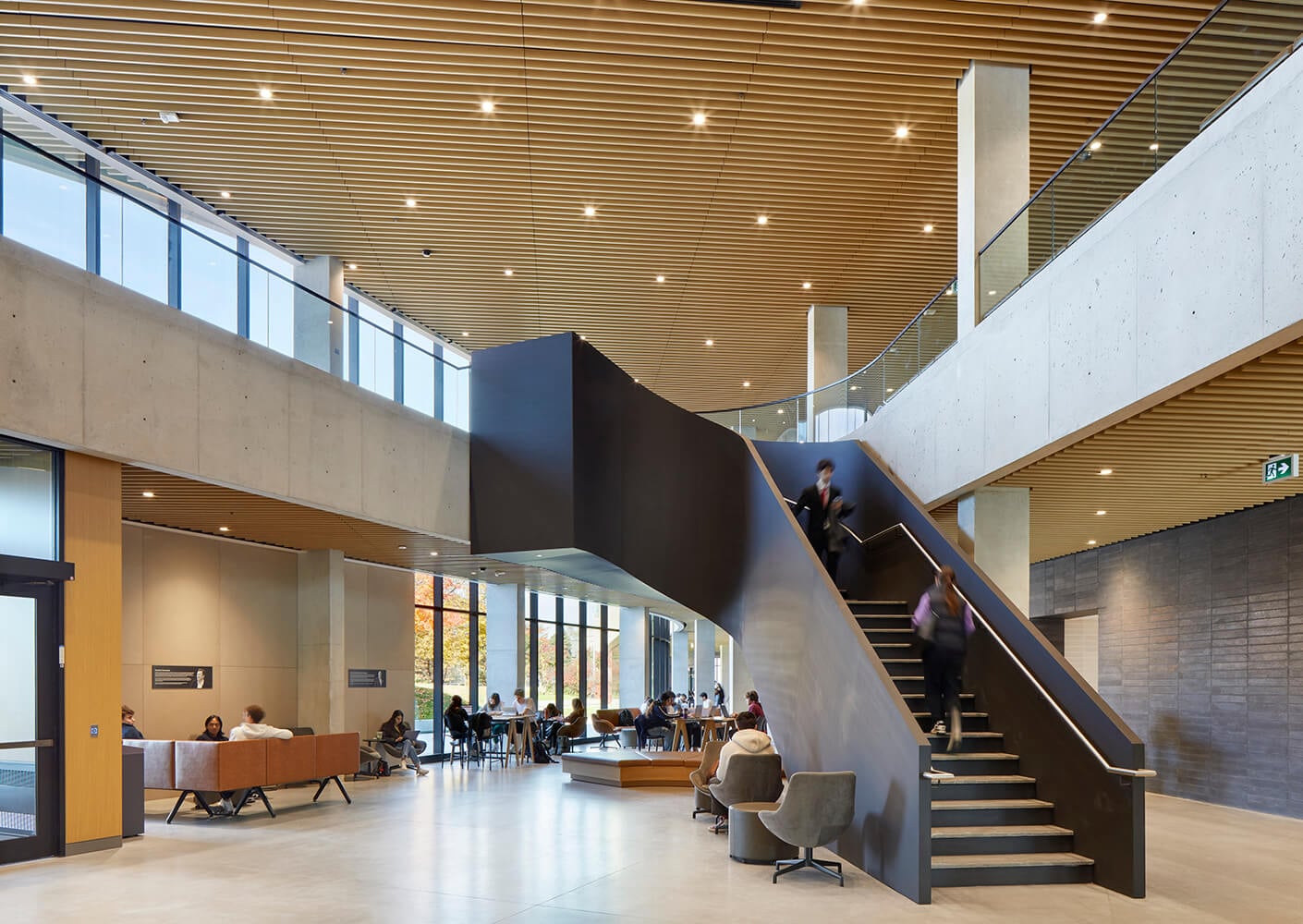 Modern university atrium with stairs, seating, and people walking and studying.