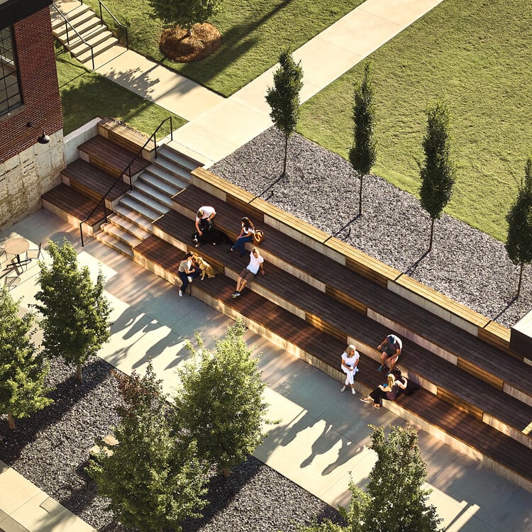 People relaxing on outdoor wooden steps surrounded by trees and shadows.