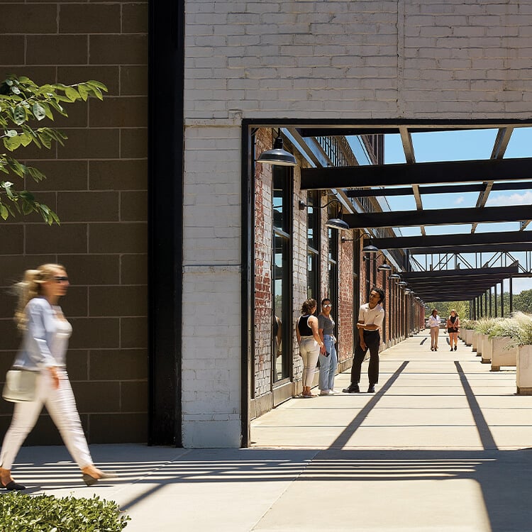 Modern industrial architecture with people walking on a sunlit outdoor walkway.