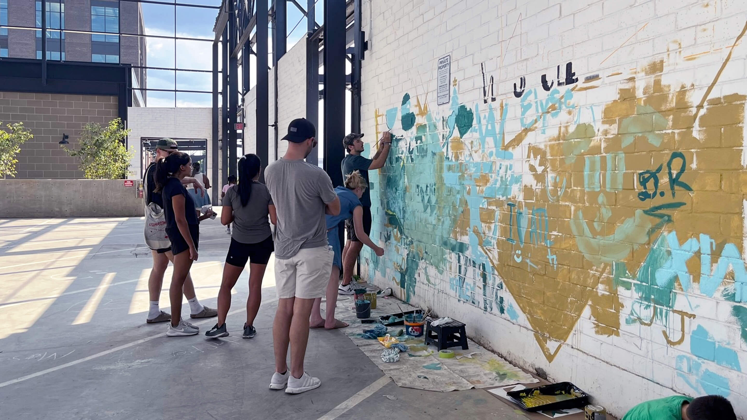 Group painting mural on urban brick wall, community art event.