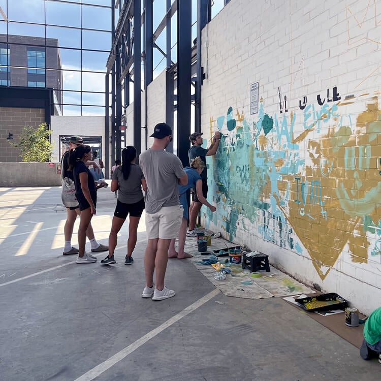People painting a colorful mural on a brick wall indoors.
