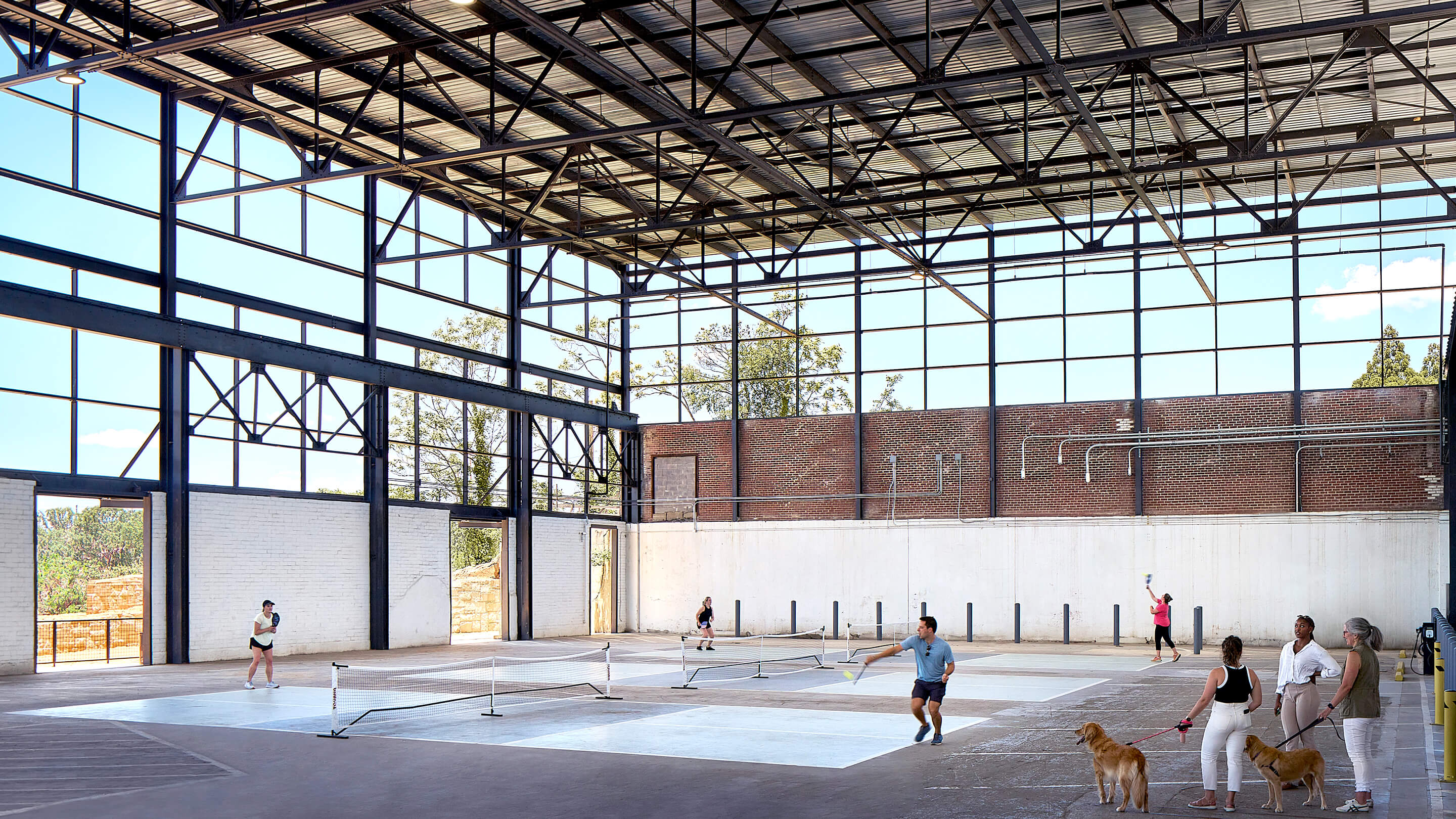 Indoor pickleball game in a spacious, sunlit industrial-style building.