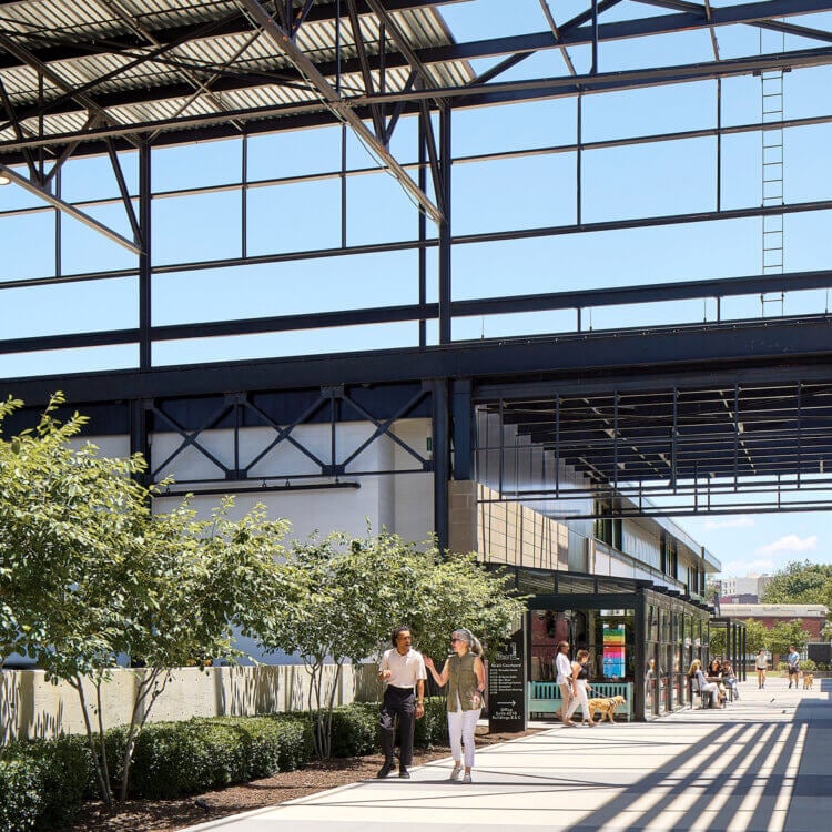 Open converted industrial space with walkway and people enjoying a sunny day.