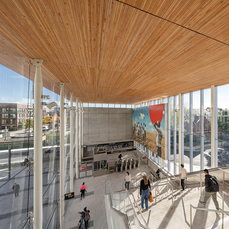 Modern train station entrance with a mural and wooden ceiling.